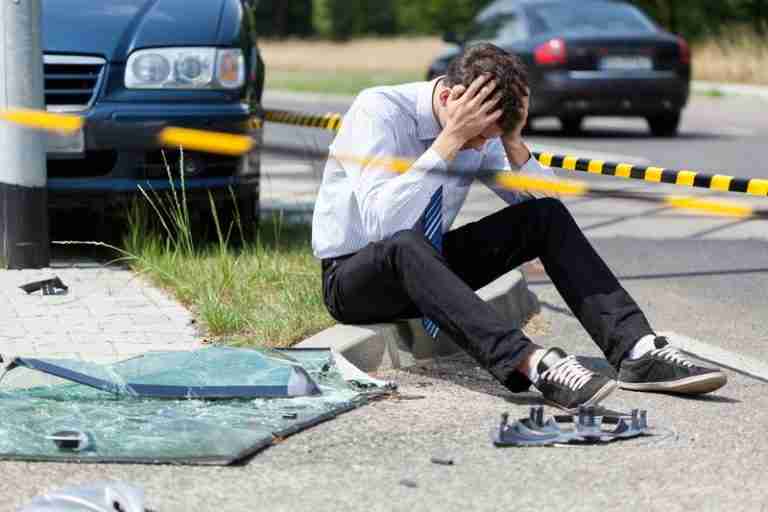 Image is of an upset man sitting on curb concept of being hit by an uninsured driver in the state of Georgia